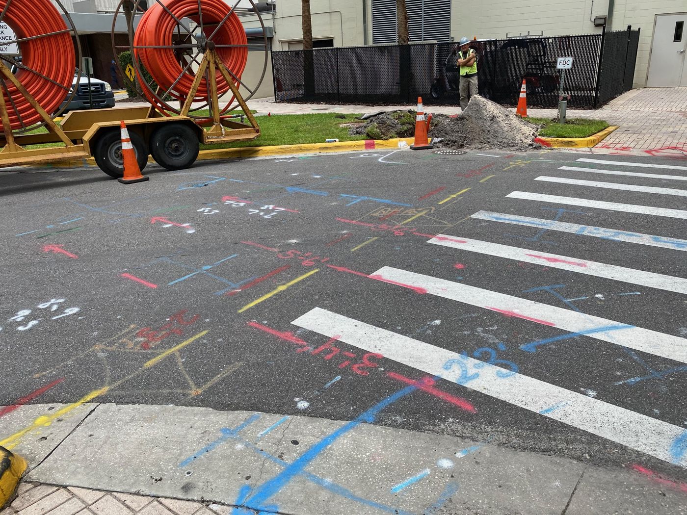 Intersection marked with utility locate paint, with conduit reels staged at the curb